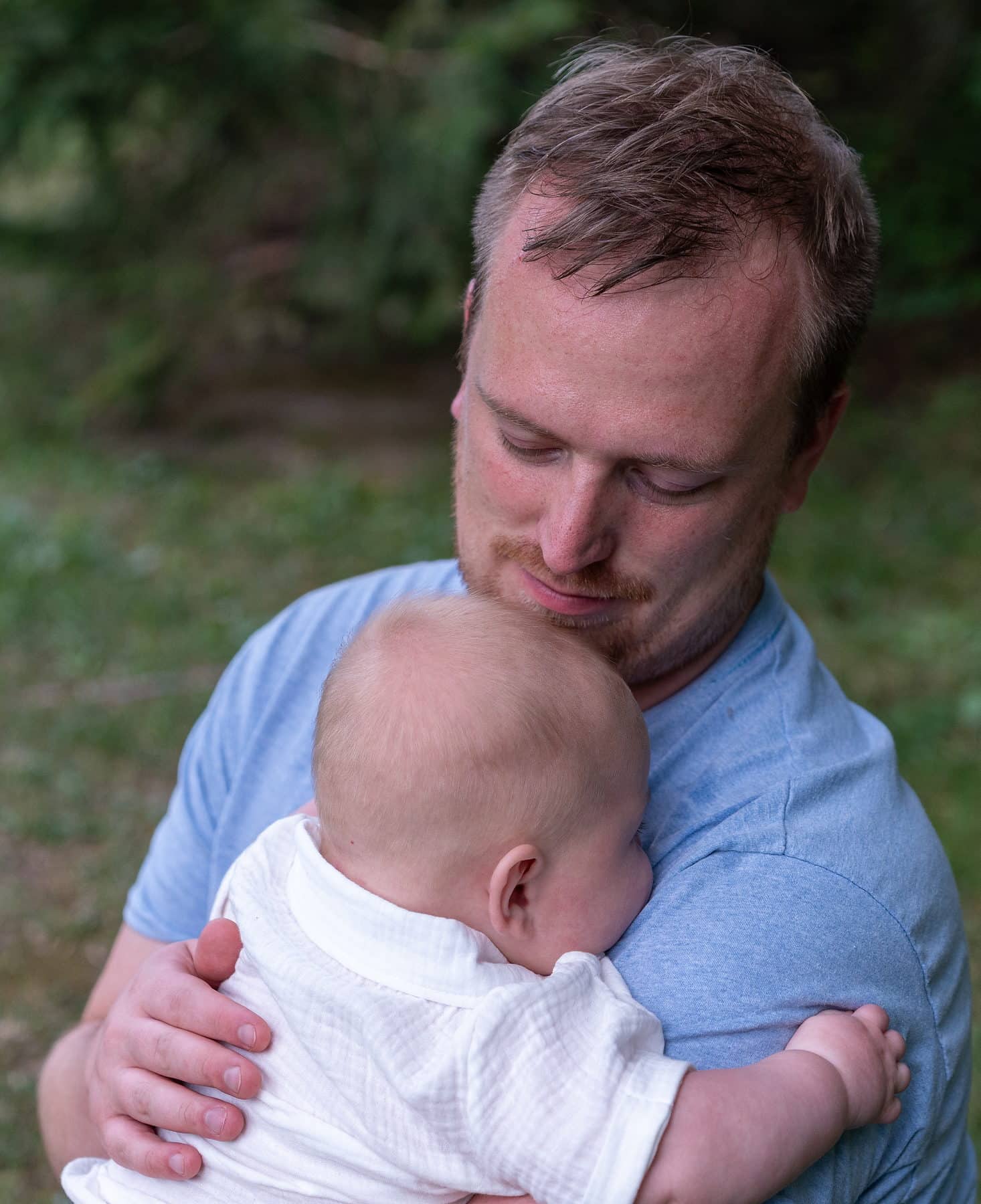 A father holding his sleeping newborn against his chest outdoors
