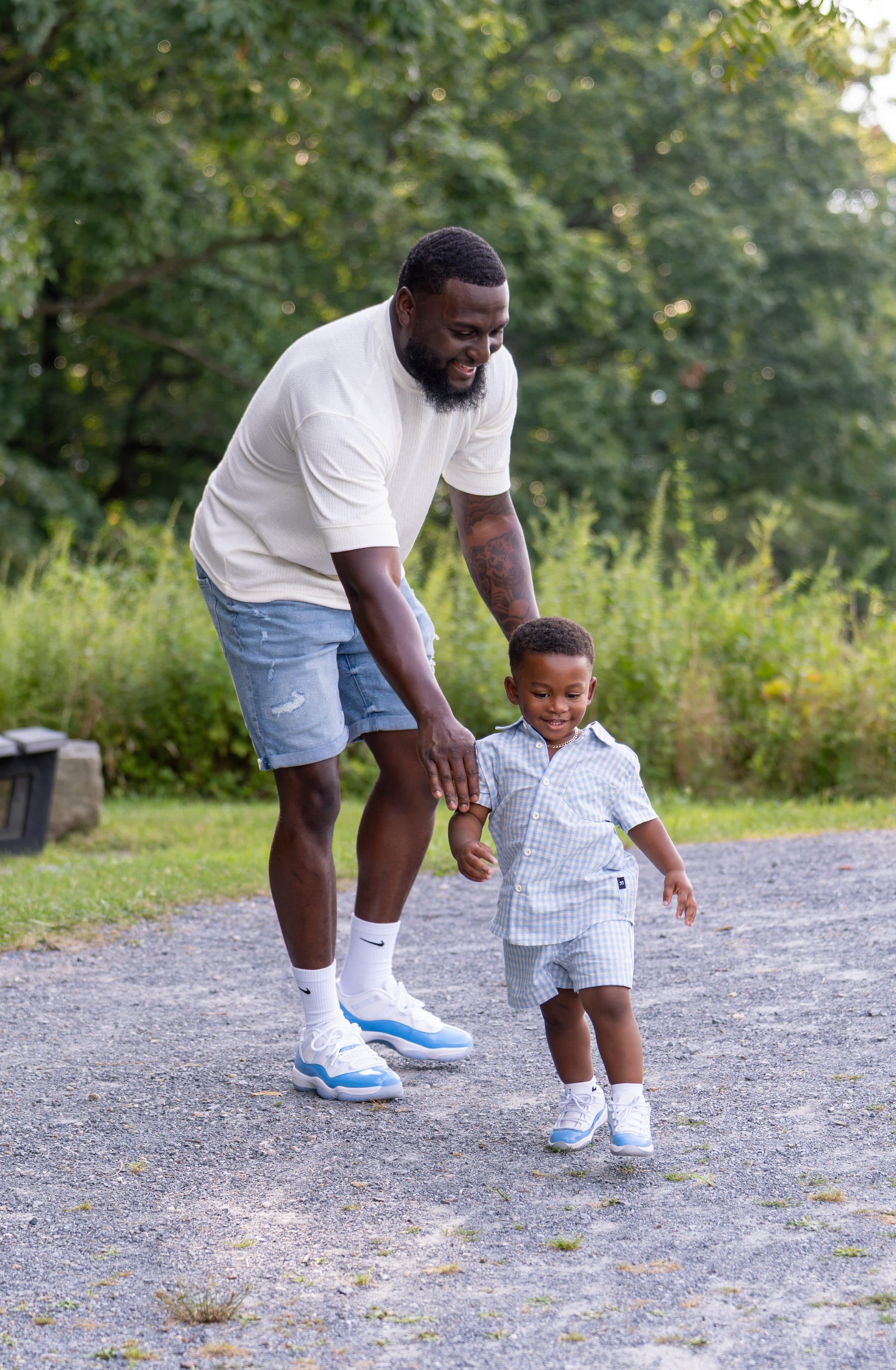 A father steadying his son's first steps on a gravel path