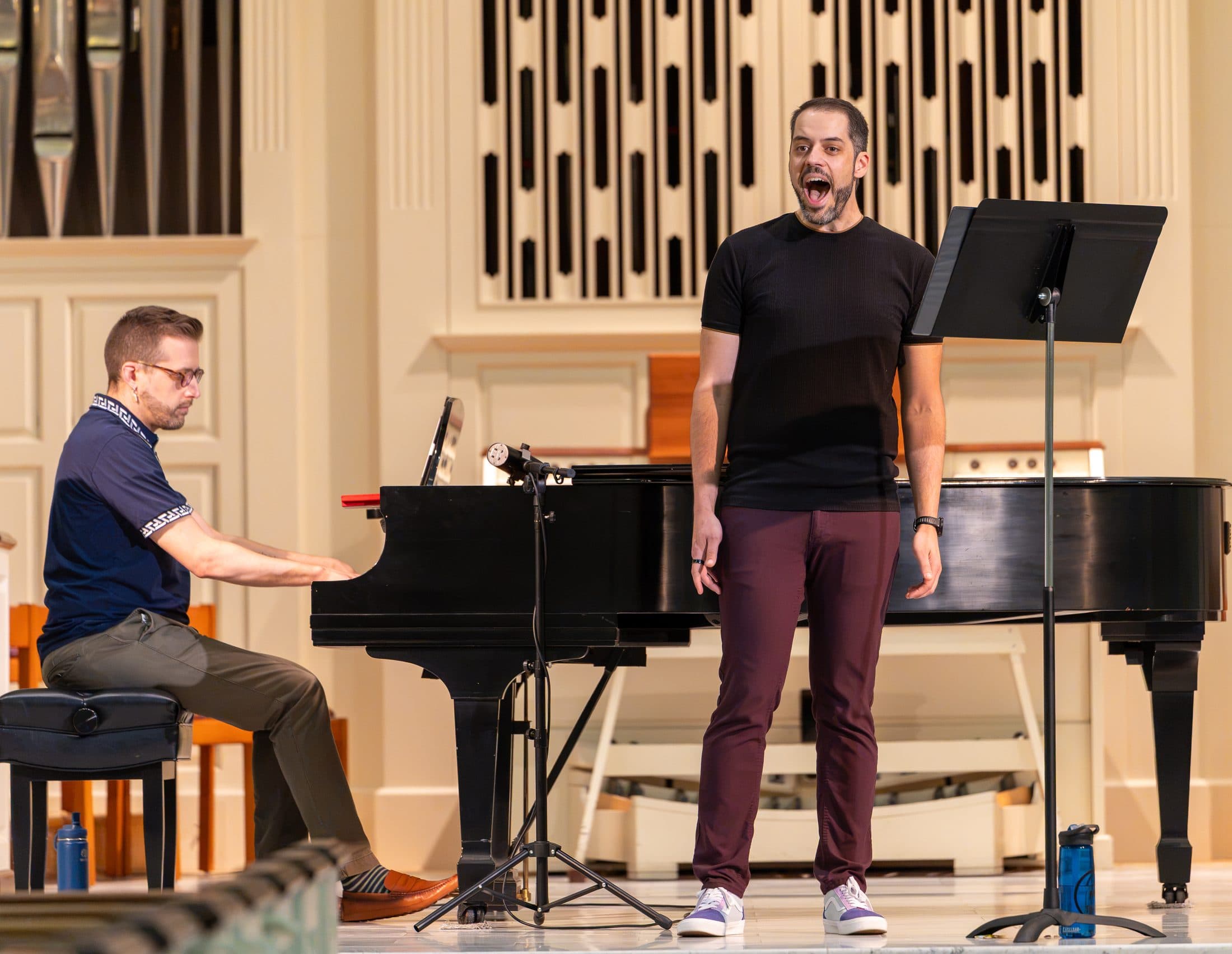 A tenor performing beside a grand piano in a concert hall